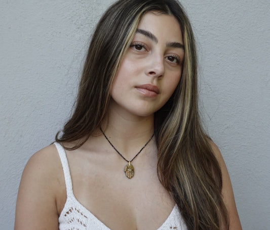 The Nëtanya Necklace: a carved golden-brown stone hamsa on fine faceted black beads