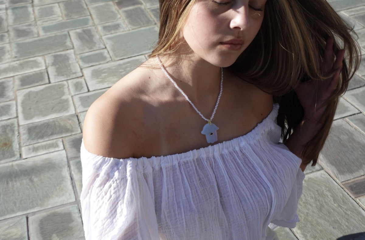 The Tël Aviv Necklace: a soft periwinkle hamsa pendant on tiny pearl-white beads